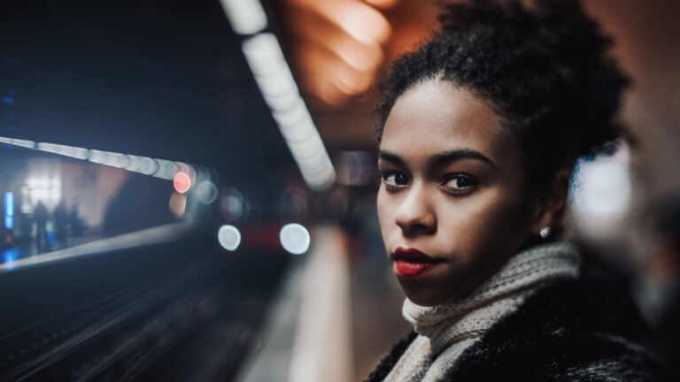 True tilt-shift portrait of a young African-American female on the platform with an arriving train in the defocused background.
