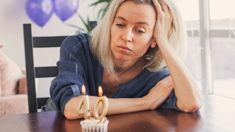 Sad lonely woman is sitting at table and looking at birthday cake. Unhappy middle age female of forty is thinking about life.