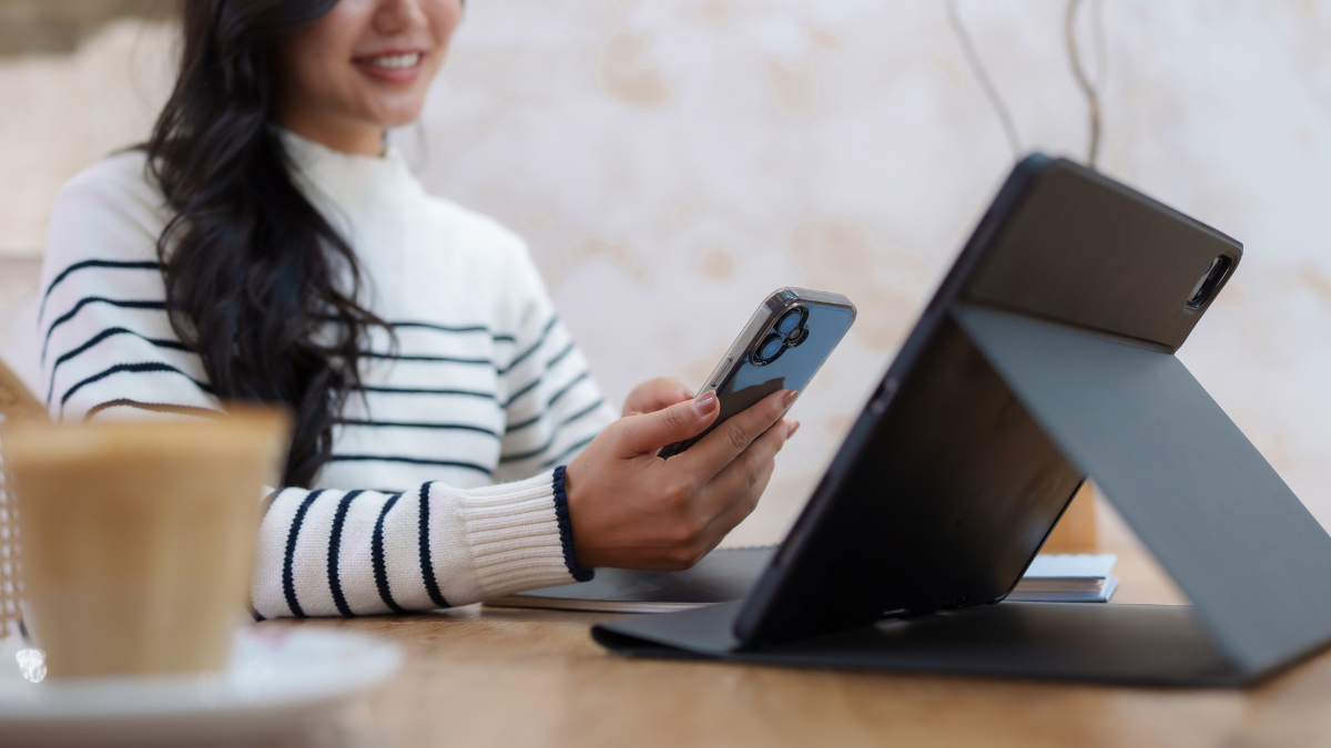 Young asian freelancer enjoying a latte while working remotely from a cozy cafe, multitasking with a smartphone and tablet, embodying a modern work life balance in an urban setting for work-life balance tips.