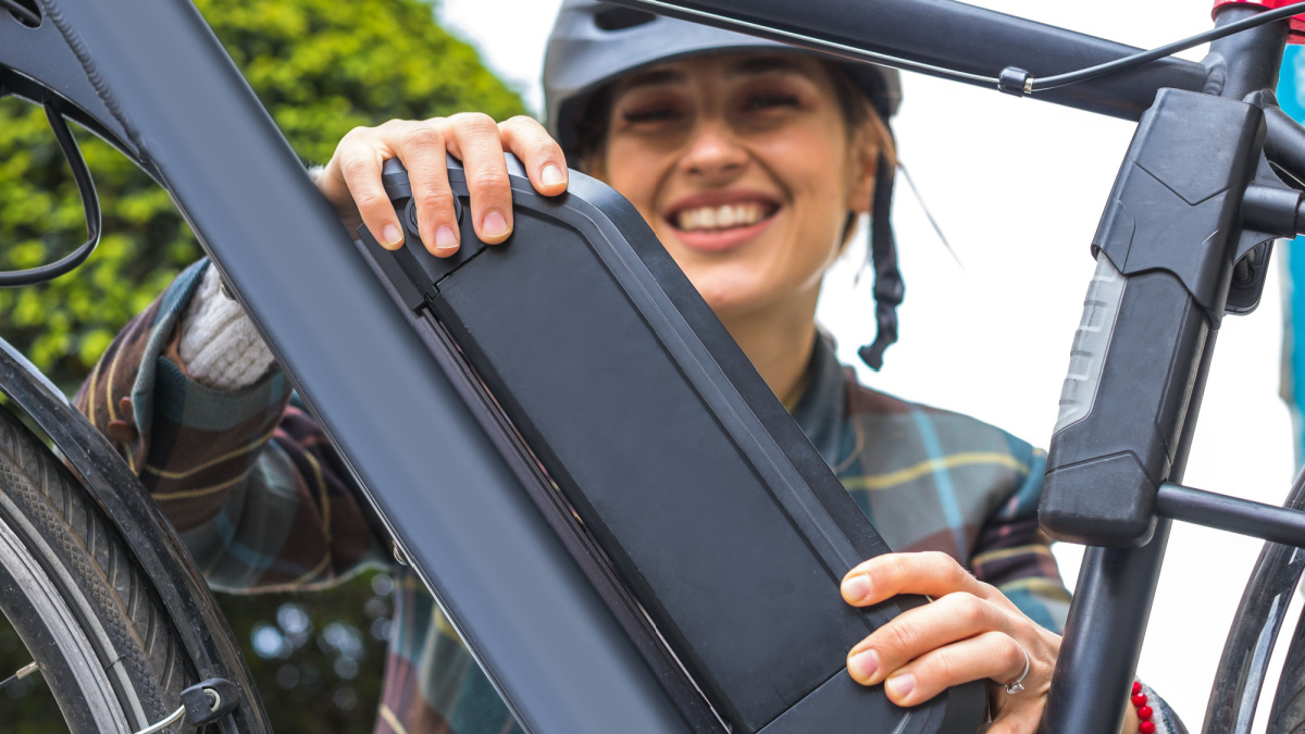 young woman holding an electric bike battery mounted on frame.