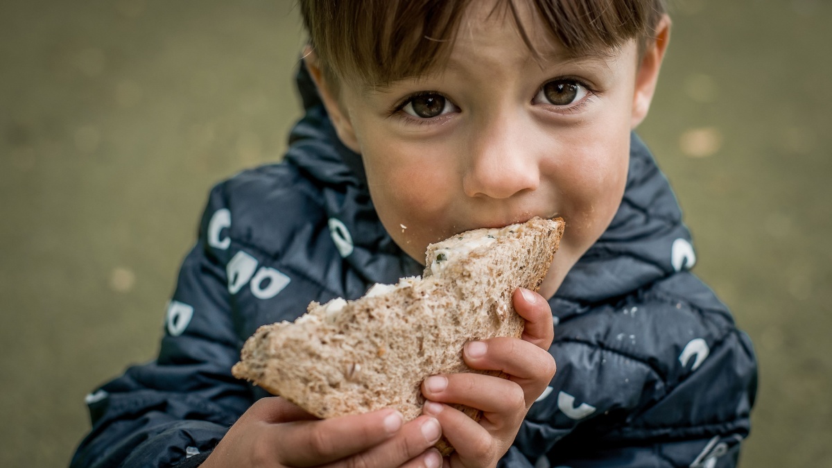 Portrait of hungry child boy looking with big eyes while eating bread. Poor refugee kid asking and looking for help. Crisis, peace, stop aggression, War in Ukraine. Sad refugee.