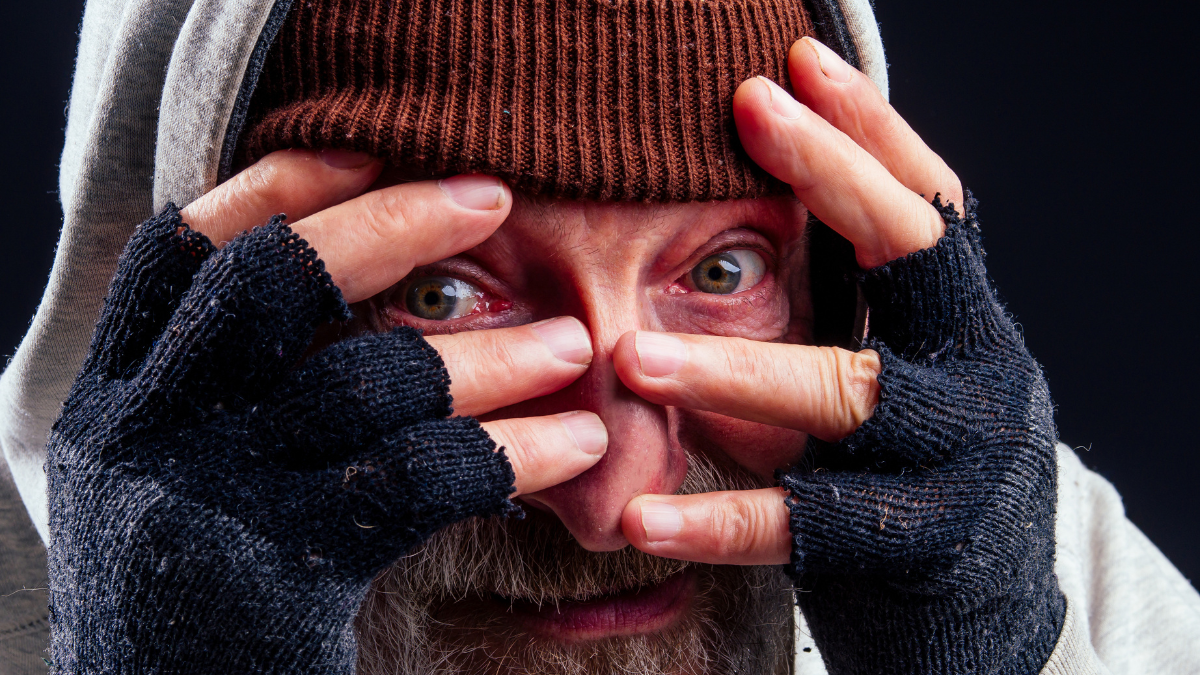 portrait of sad old senior male tramp wearing warm brown hat and leaky gloves,holding metal canned bank jar for money alms in studio black background.