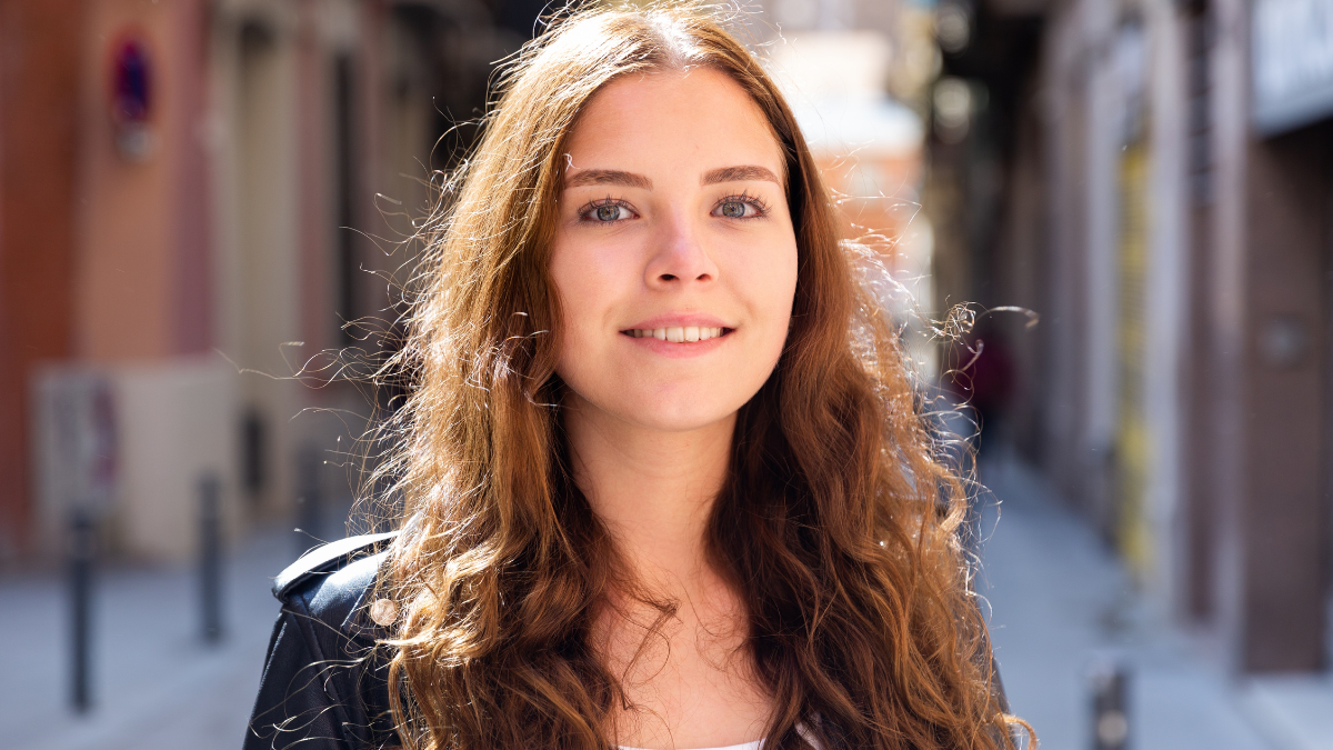 Portrait of a positive confident girl, standing in good weather on the street.