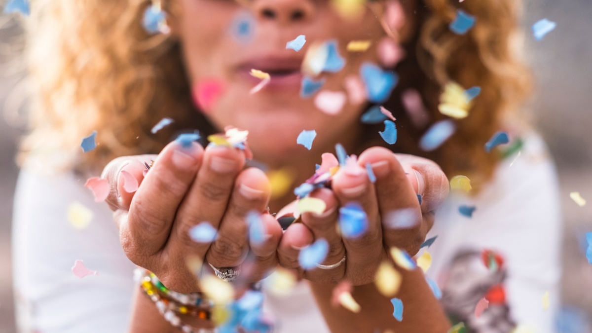 beautiful defocused woman blow confetti from hands. celebration and event concept. happiness and coloured image.