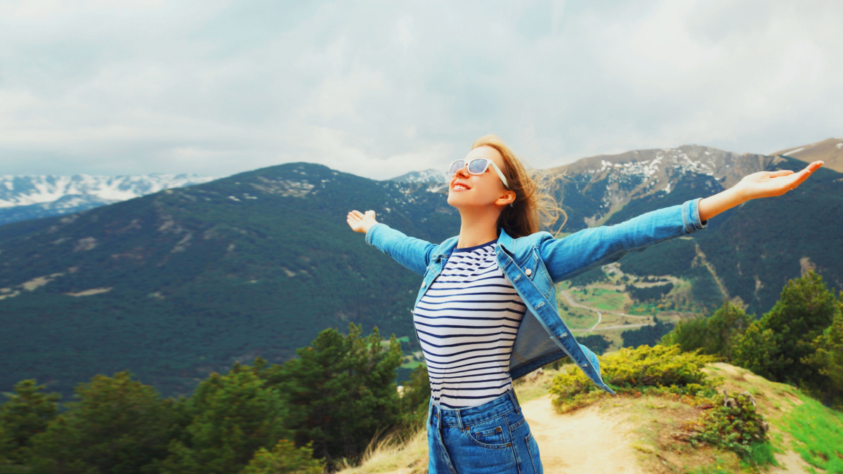 Travel concept, happy woman enjoying fresh air mountains raising her hands up on Andorra mountain background.