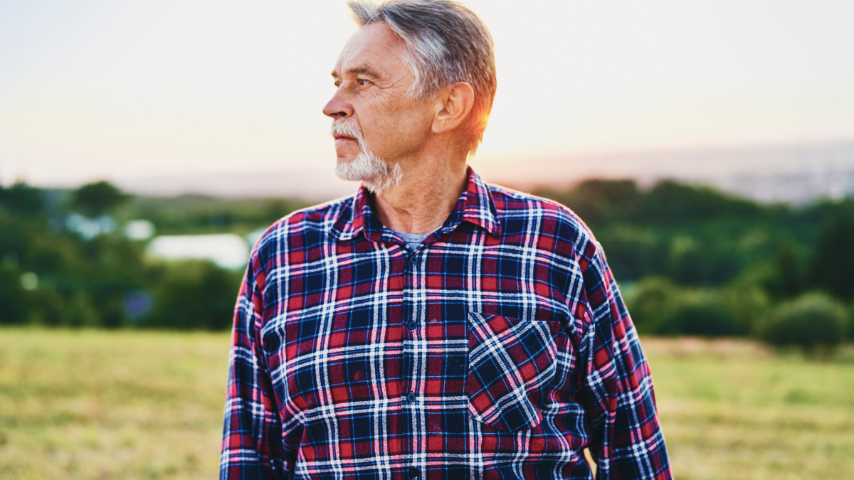 Senior man looks over his land at sunset.