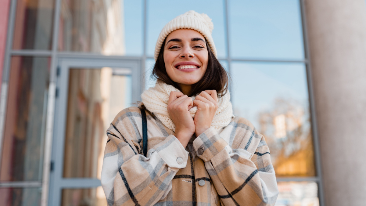 stylish attractive young smiling woman walking in street in winter outfit with coffee wearing checkered coat, white knitted hat and scarf, happy mood, fashion style trend.