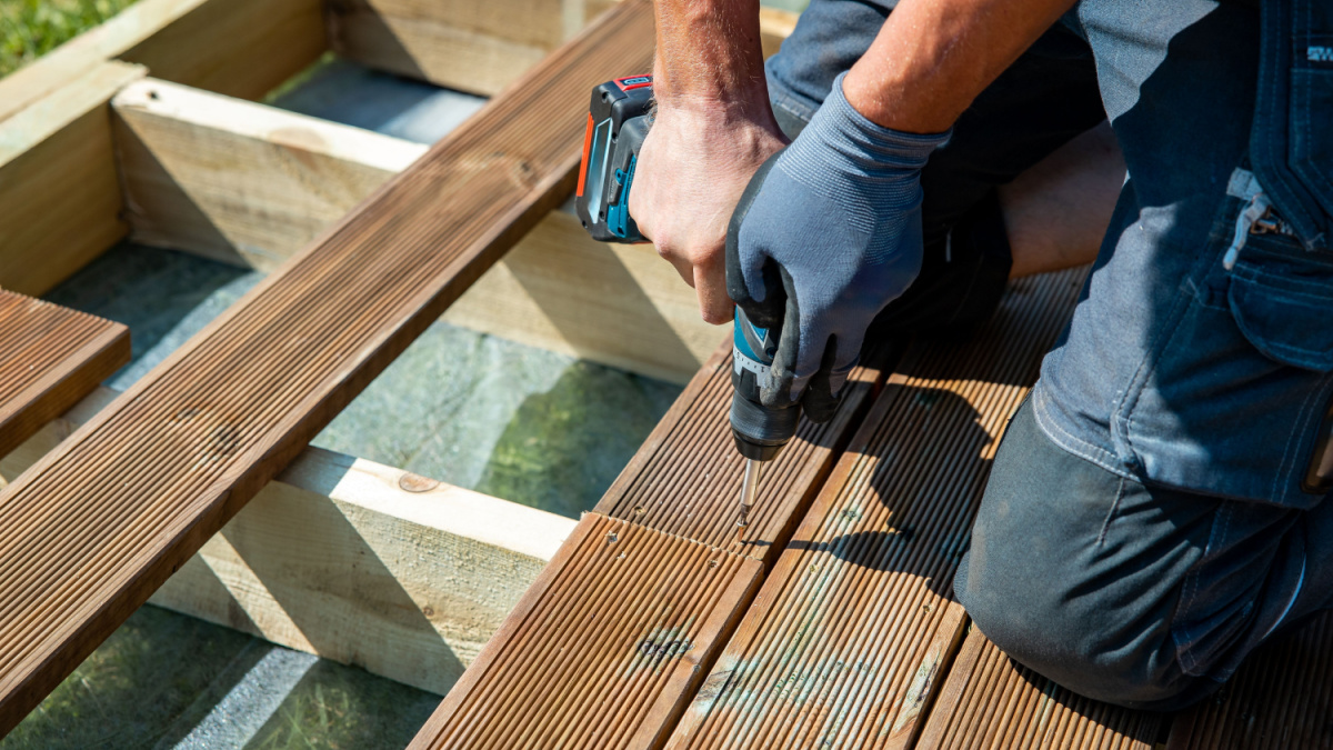 Deck construction, builder hand with electric screwdriver installing impregnated wooden boards.