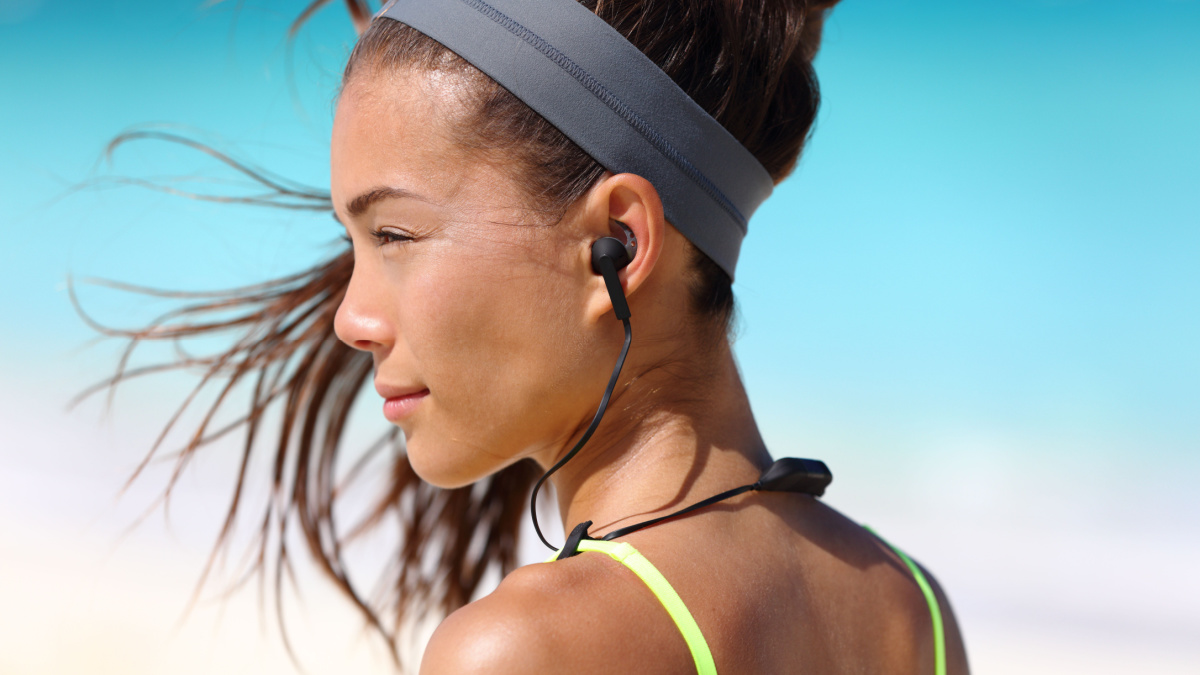 Fitness girl with sport in-ear wireless headphones. Asian female athlete woman runner wearing Bluetooth earphones with wing tip design for sports activities.