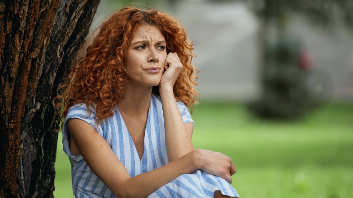 Sad young woman with red hair looking away in park.