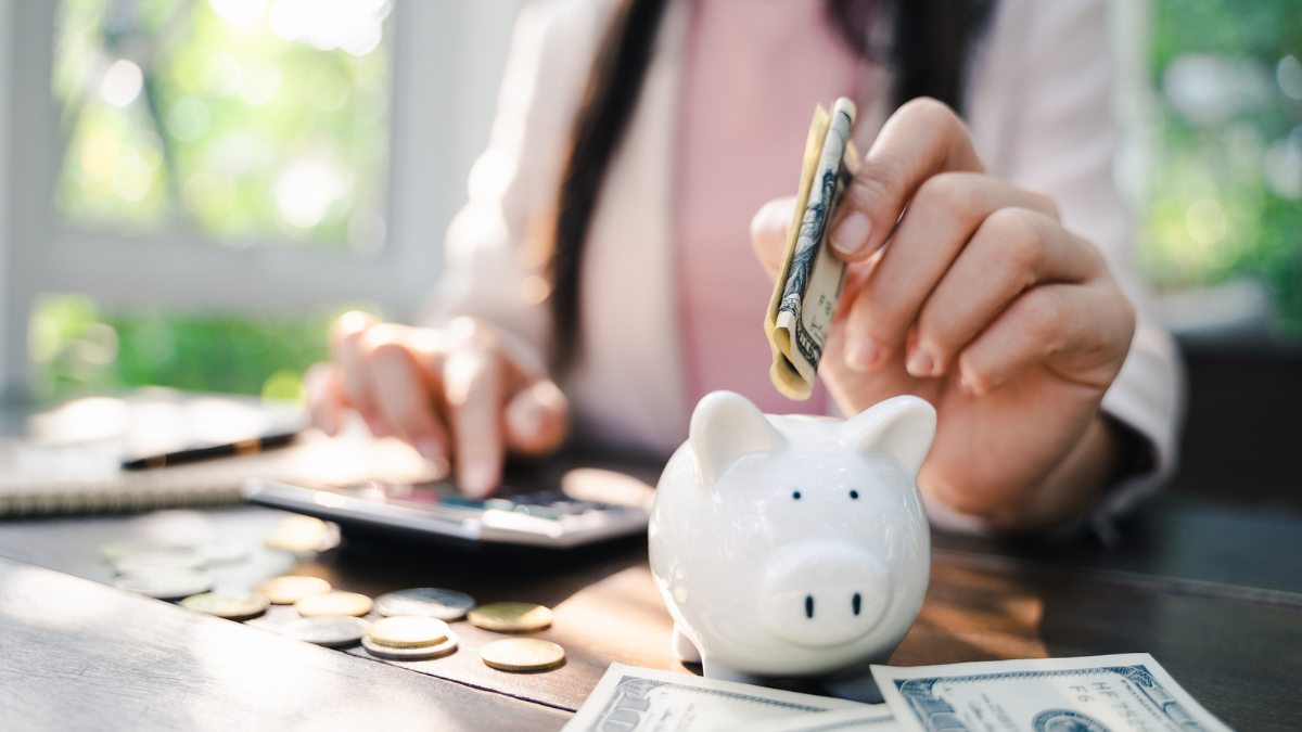 Closeup of business woman hand putting money into piggy bank for saving money.