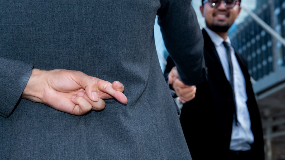 man shake hands together and holding another fingers crossed behind his back