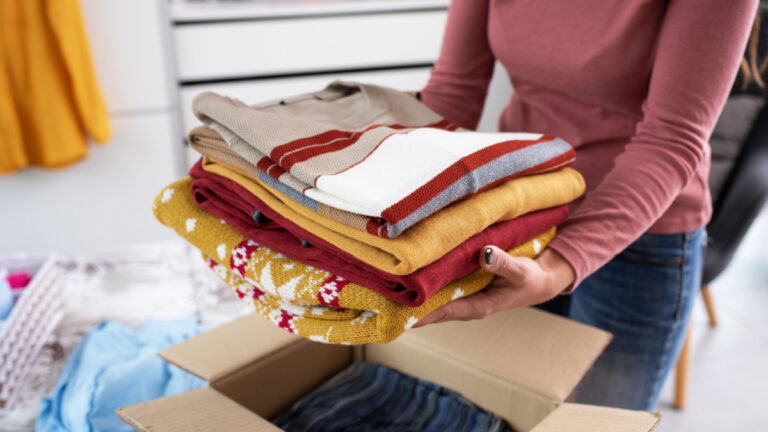 Young woman folding her clothes and packing them in a delivery box, she is changing her wardrobe.