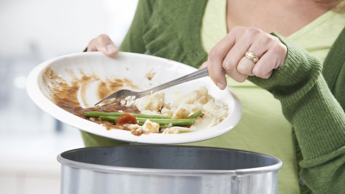 Woman Scraping Food Leftovers Into Garbage Bin.