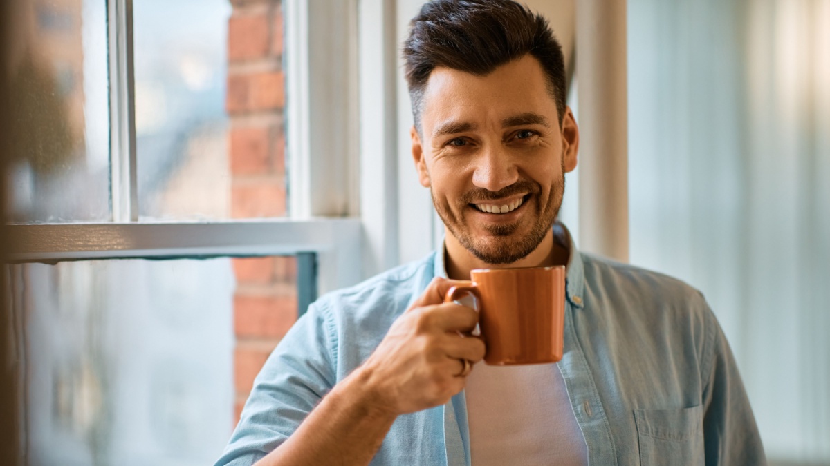 Happy man drinking coffee at home and looking at camera.