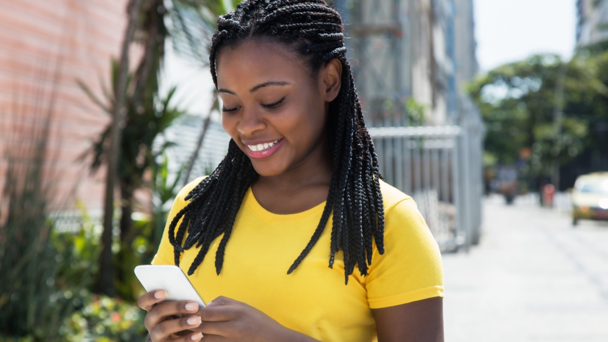 Beautiful african american woman in a yellow shirt texting message with mobile phone.