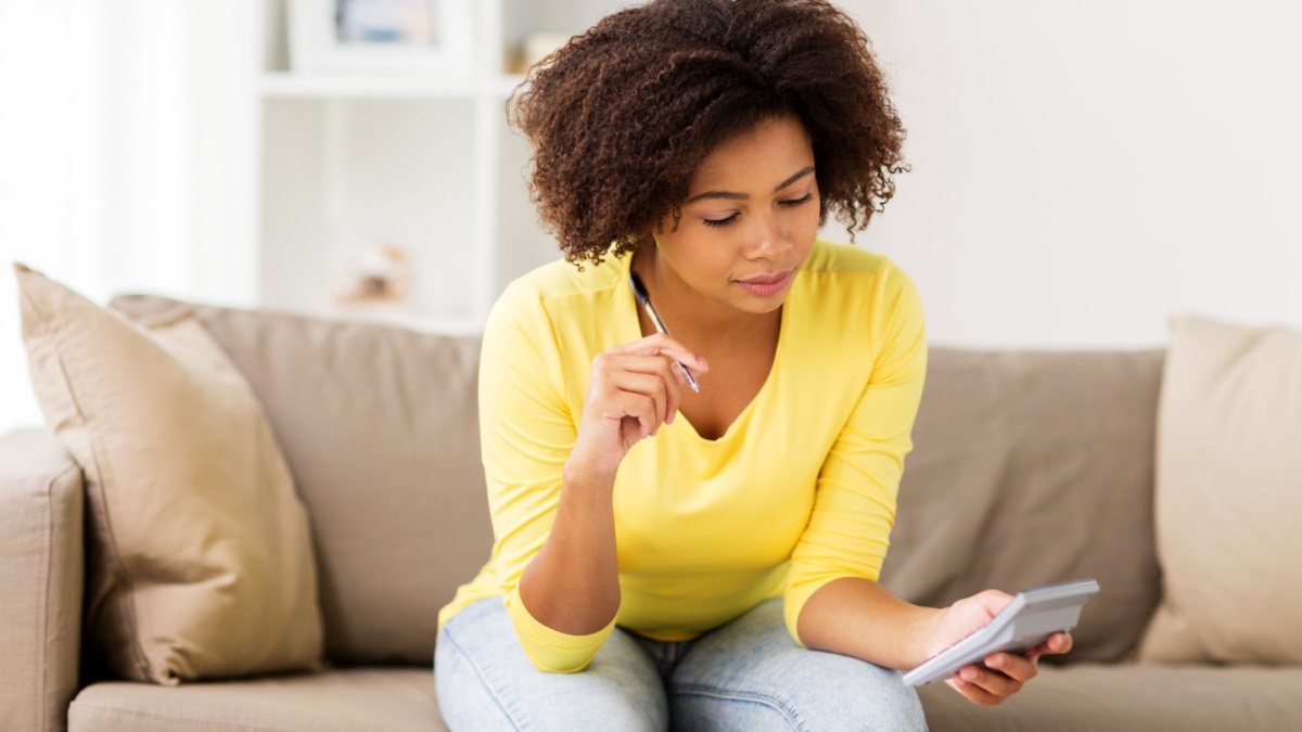 budget, finances and people concept - african american woman with papers and calculator counting money at home.