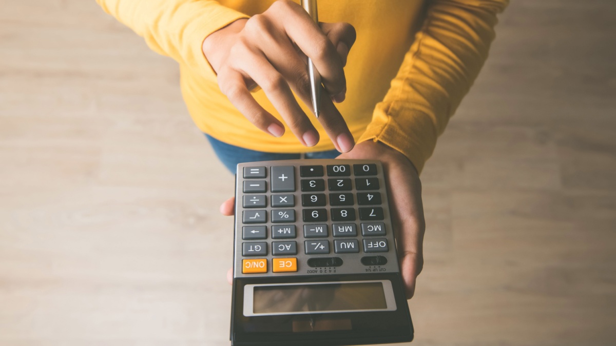Woman entrepreneur using a calculator with a pen in her hand, calculating financial expense at home office.