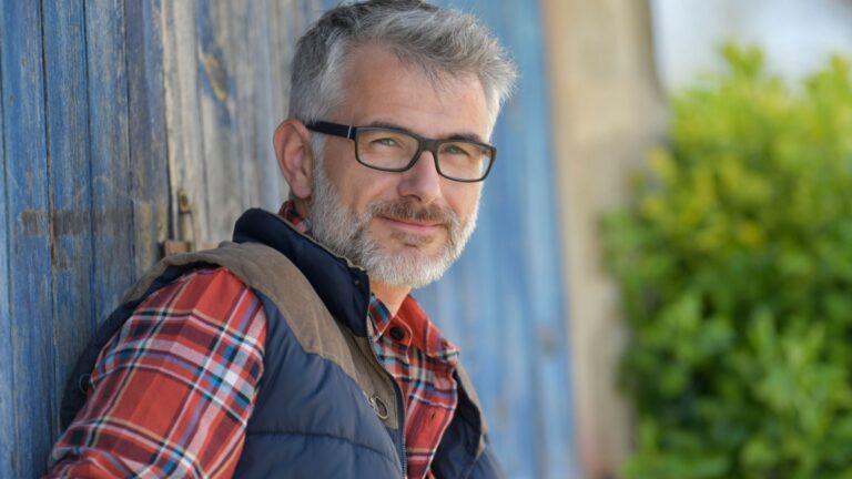 Portrait of farmer leaning on cowshed door.