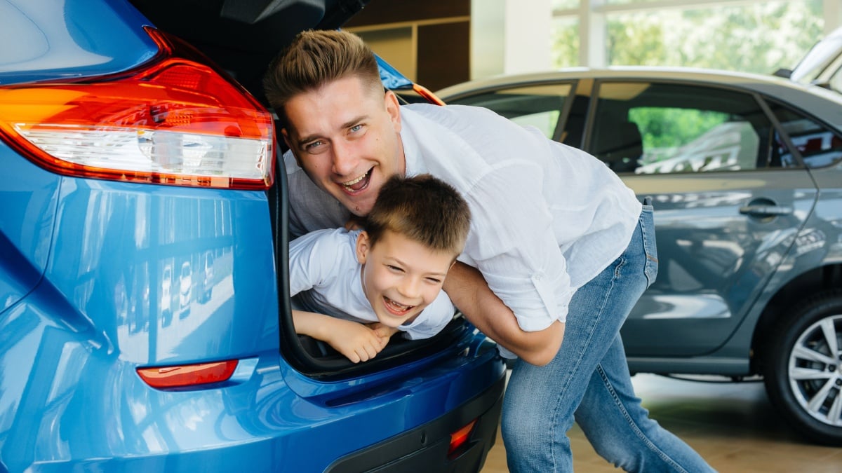 A little boy sits in the trunk while his parents choose a new car.