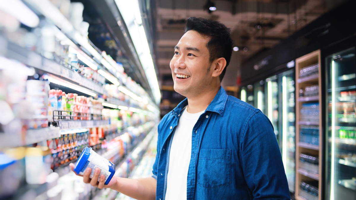 Happy Asian man in casual blue shirt shopping in supermarket.