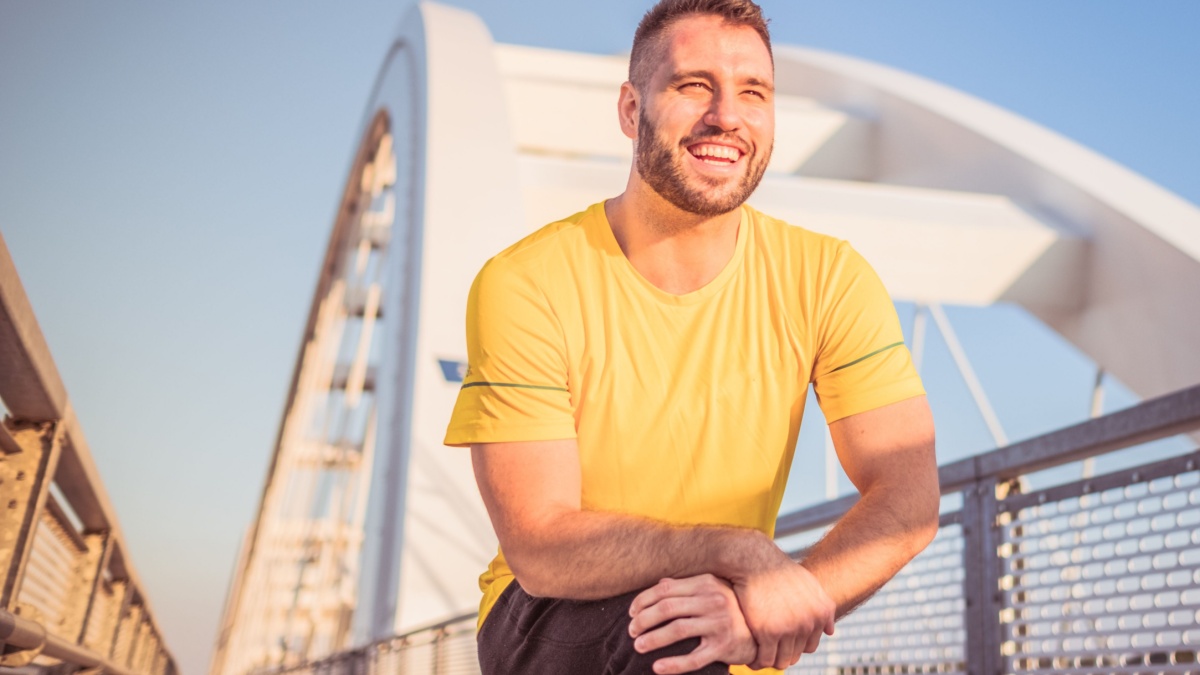 Young handsome man exercising outdoors and smiling. Wearing yellow shirt.