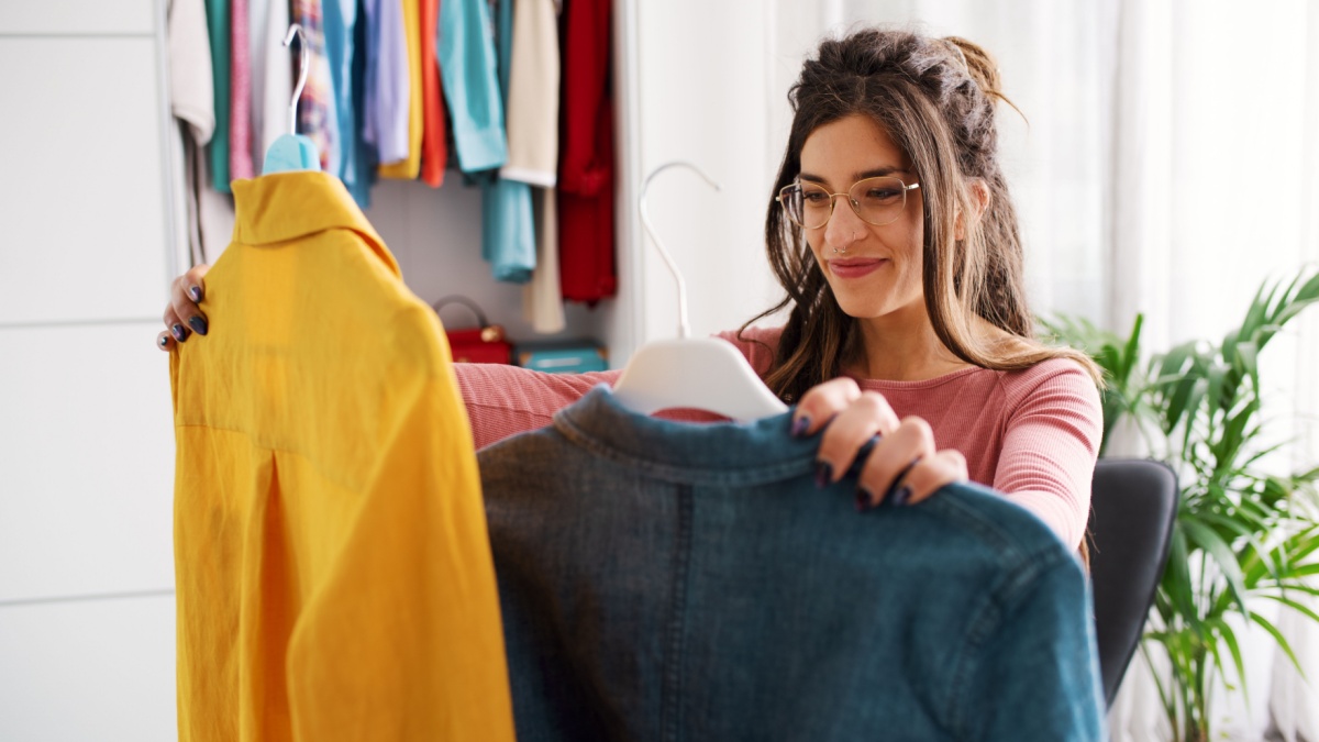 Young happy woman holding two shirts and comparing them, she is choosing what to wear.