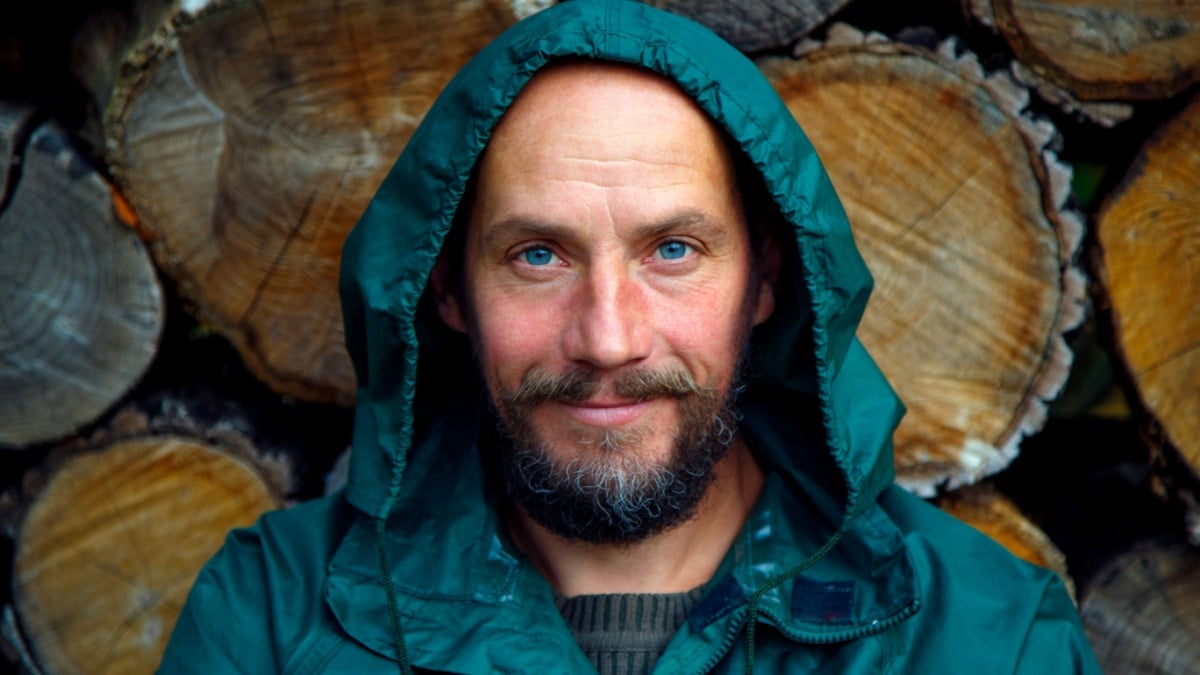 Portrait of a bearded man on a background of firewood. A bearded man poses for the camera after cutting firewood in the forest.