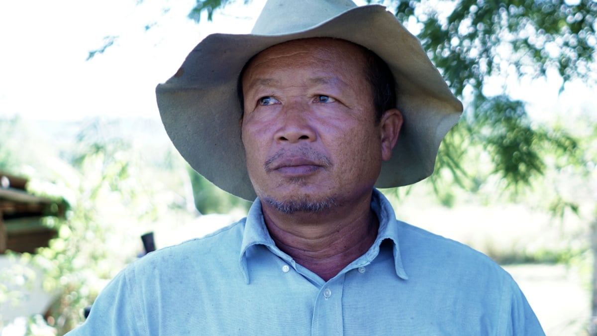 An elderly man standing in a cowboy hat native to Thailand taking a close-up of his face.