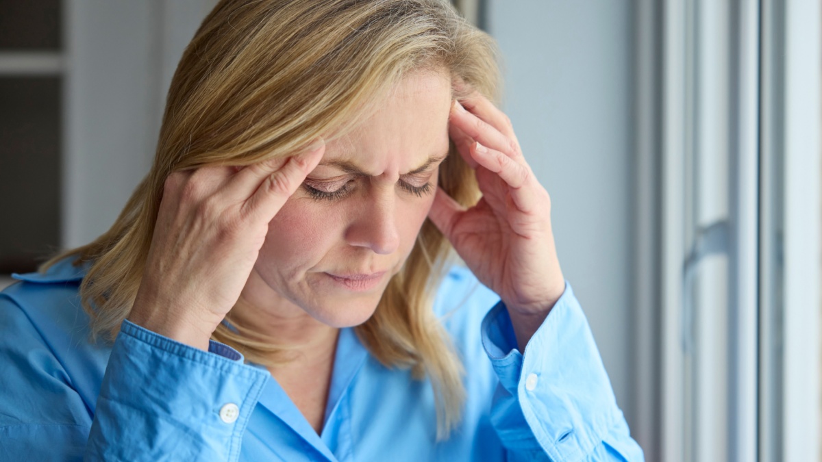 Menopausal Mature Woman At Home Standing By Window Suffering With Headache Or Migraine Pain.