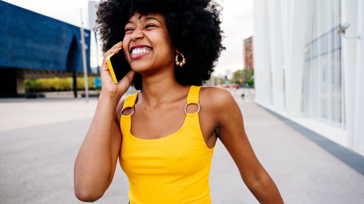Beautiful young happy african woman with afro curly hairstyle strolling in the city - Cheerful black student girl walking on the street.