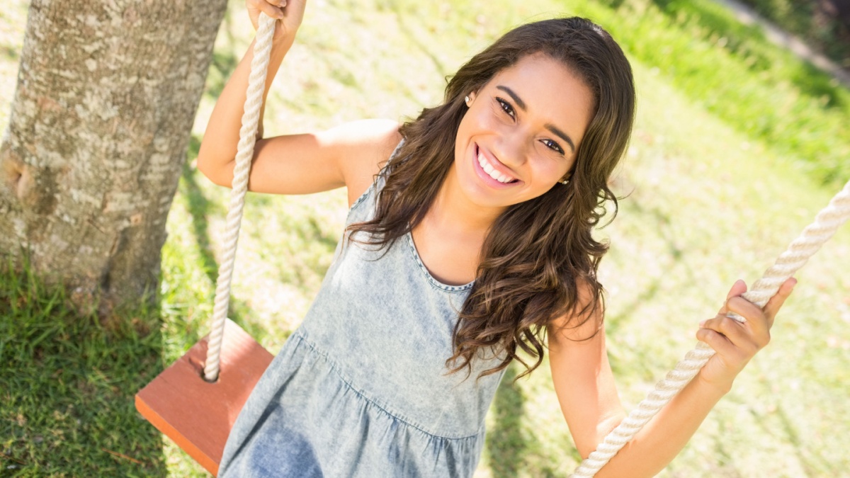 Pretty brunette swinging in park on a sunny day.