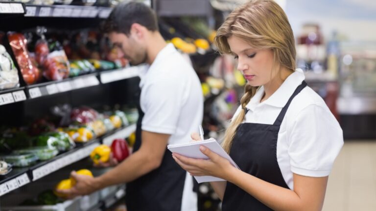 Serious staff woman wrting on notepad at supermarket.