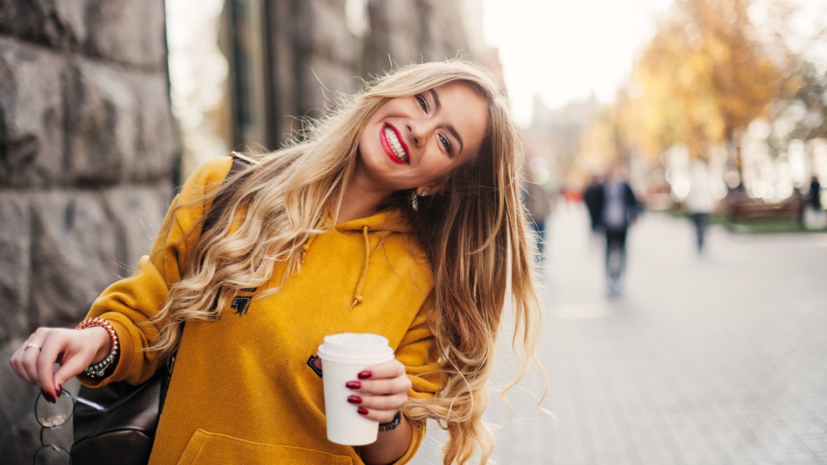 Stylish happy young woman wearing boyfriend jeans, white sneakers bright yellow sweatshirt.