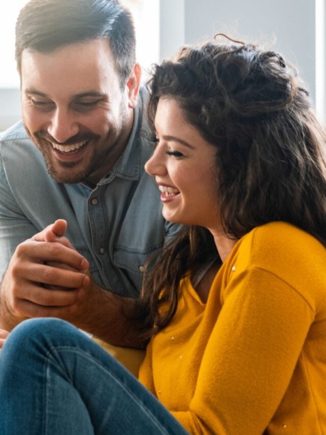 Cheerful couple using mobile phone at home stock photo.