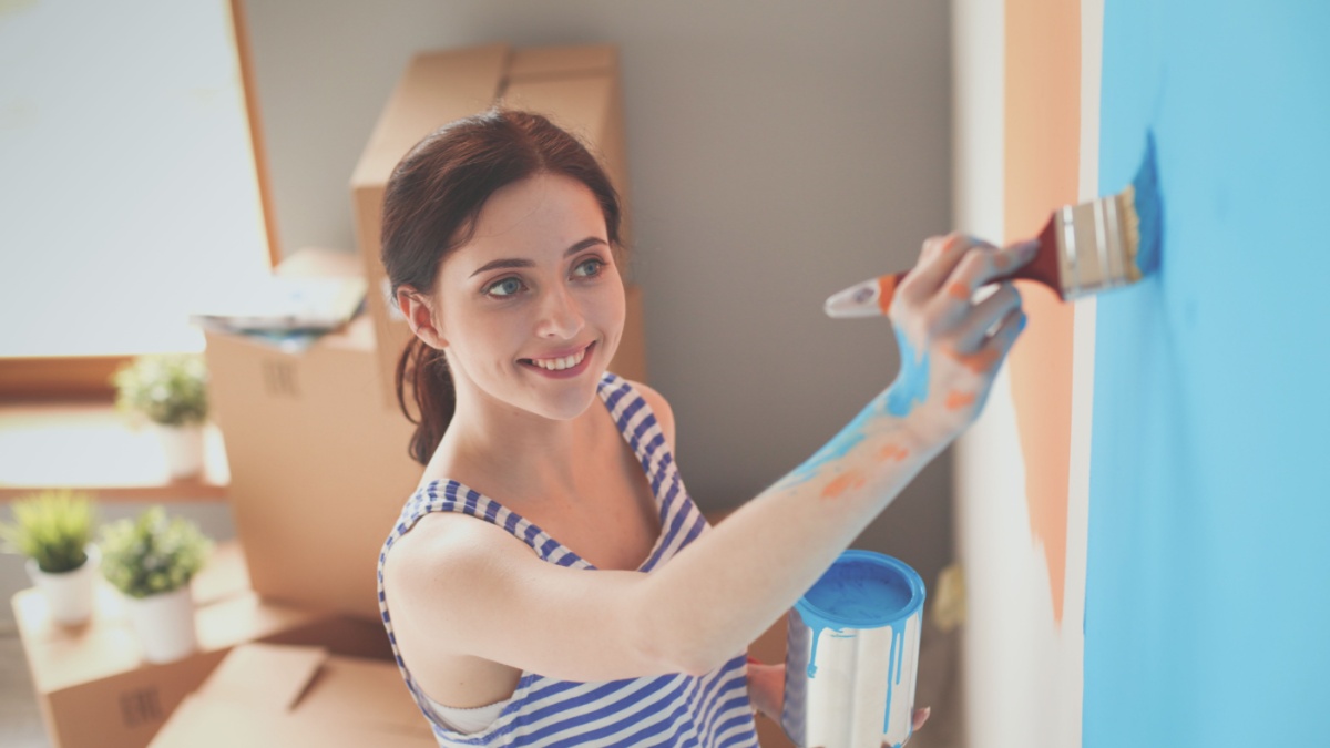 Happy smiling woman painting interior wall of new house. Happy smiling woman.