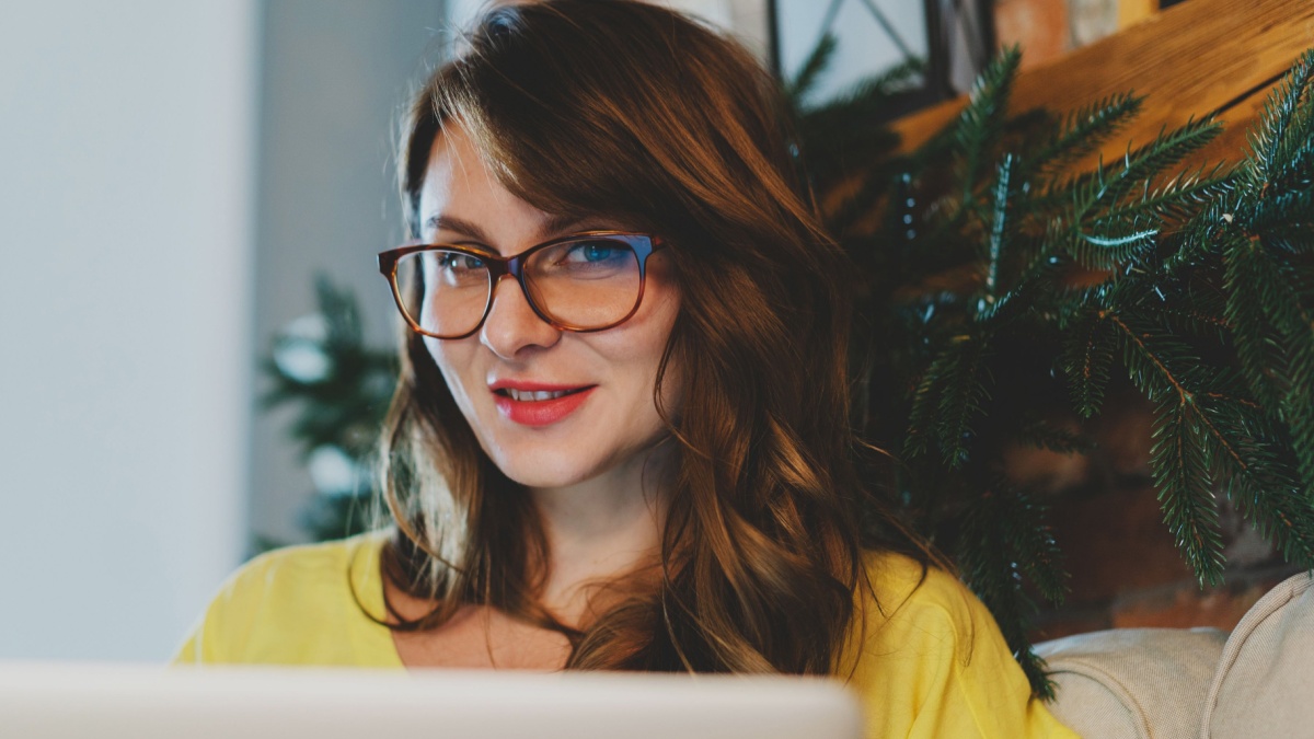 Portrait of female blogger wearing glasses using laptop at home. Beautiful woman sitting on the sofa and working on her laptop computer.