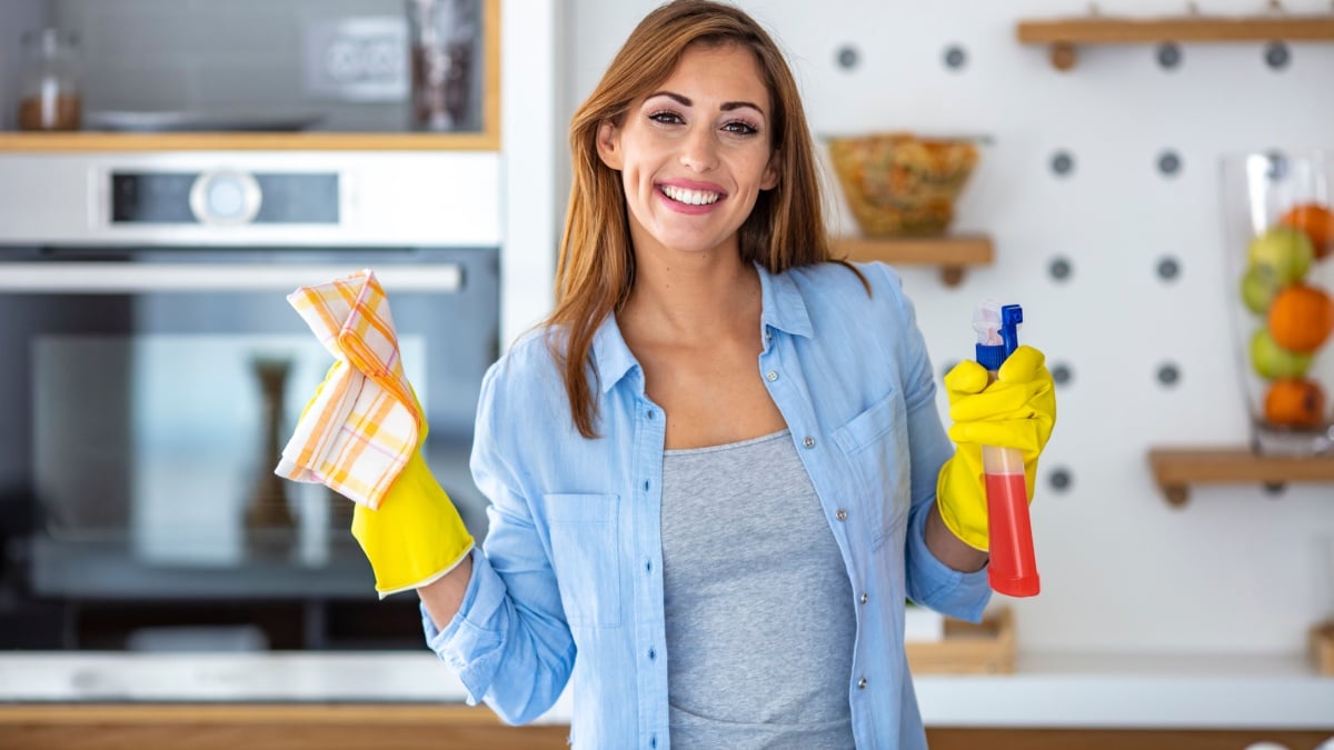 Young woman doing house chores. Woman holding cleaning tools. Woman wearing rubber protective yellow gloves, holding rag and spray bottle detergent.