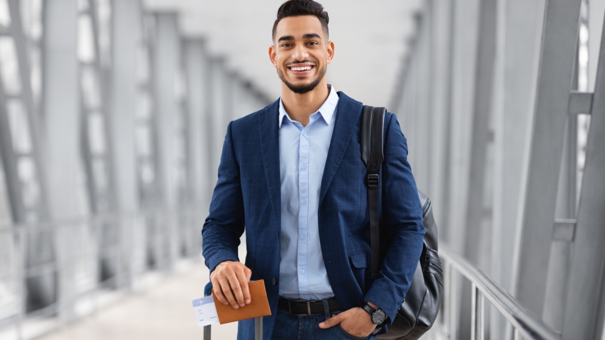 Portrait Of Young Middle Eastern Male Traveller Posing At Airport, Handsome Arab Man With Luggage, Passport And Tickets Smiling At Camera While.