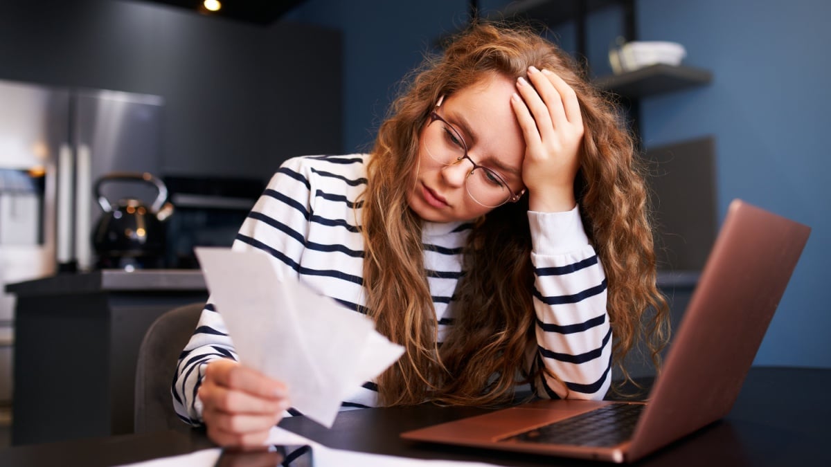 Unhappy woman calculates expenses on bills, upset about increased utilities prices. Female counting paychecks, debts, loans, reciepts to pay taxes.