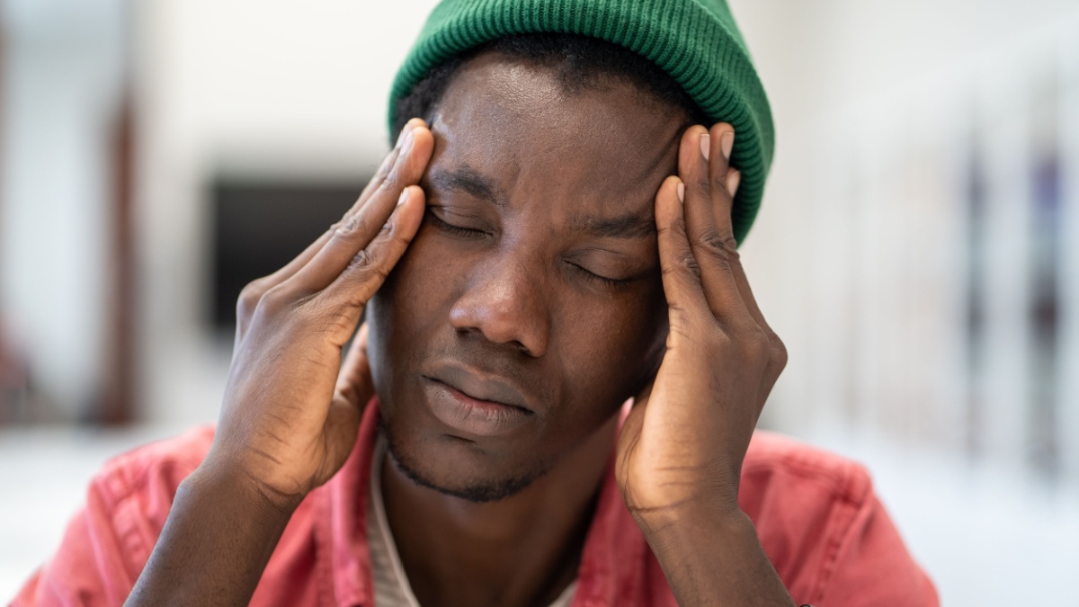Depressed tired perplexed of problem African American man freelancer sit with closed eyes touch head with hands feels unwell.