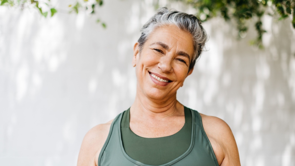 Mature woman looking at the camera with a happy smile as she takes on her outdoor workout routine in the morning. Retired woman staying healthy and active by adding regular exercise to her lifestyle.