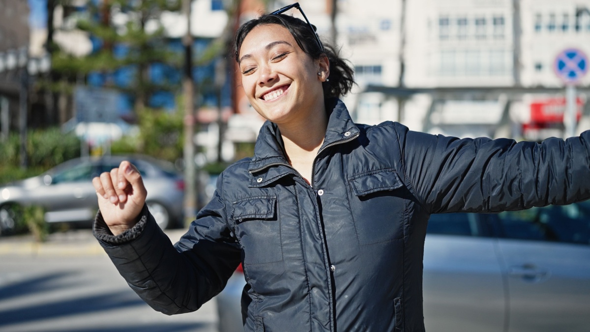 Young beautiful hispanic woman dancing listening to music on smartphone at street.