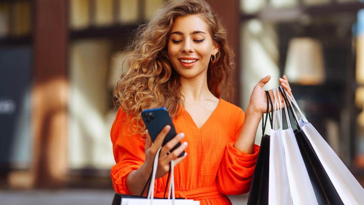 Happy female tourist doing shopping using smartphone while walking in sunny european city.