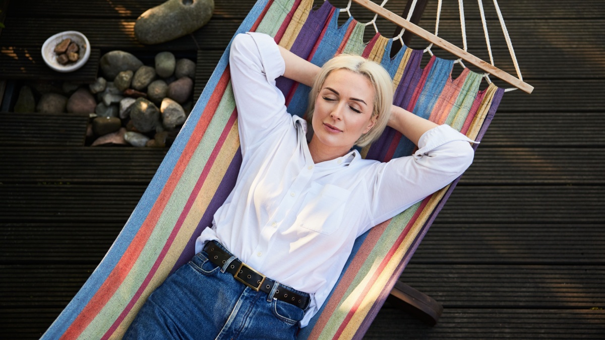 Adult woman sleeping in hammock on deck terrace during sunny summer afternoon. Healthy nap habit concept.