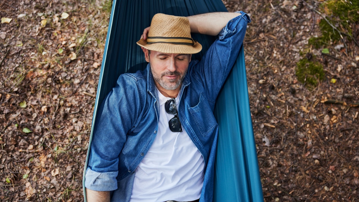 Overhead portrait of handsome adult man sleeping in hammock in forest taking nap during hiking trip.