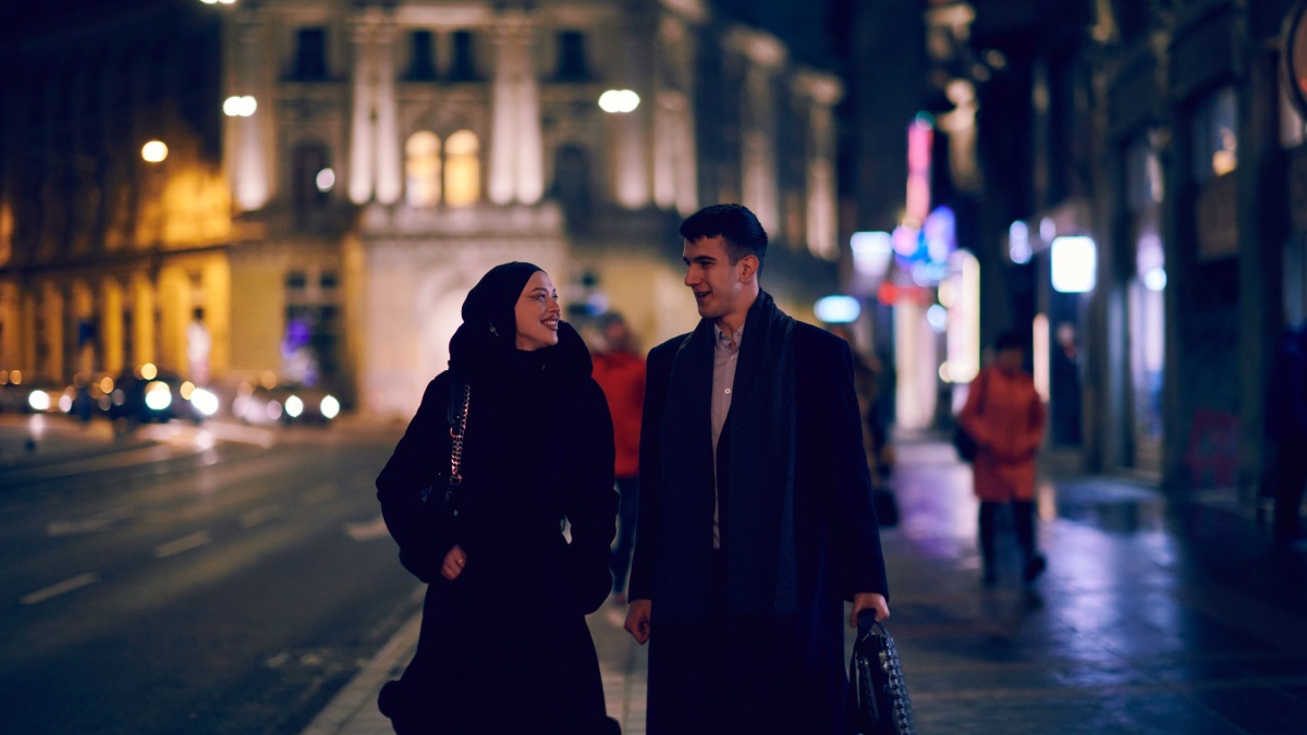Happy multicultural business couple walking together outdoors in an urban city street at night near a jewelry shopping store window.
