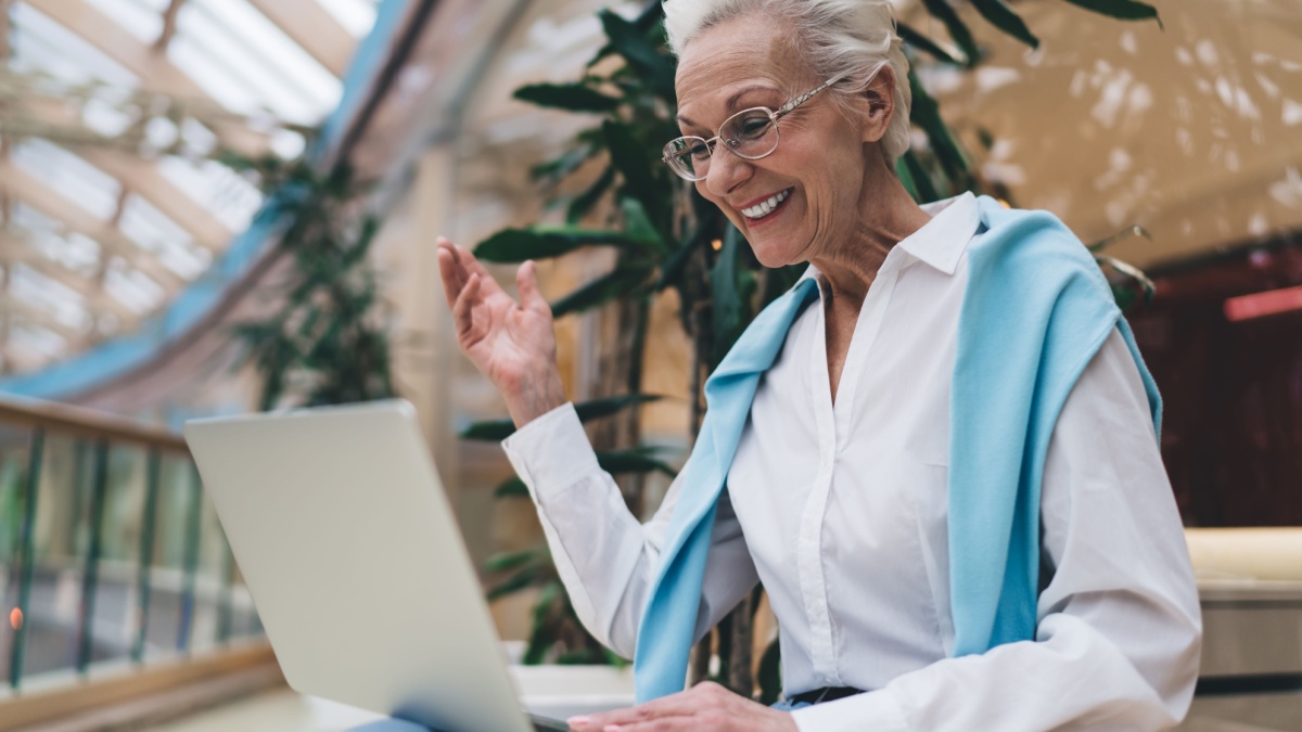 Elderly Caucasian woman in her 70s, smiling joyfully using laptop.