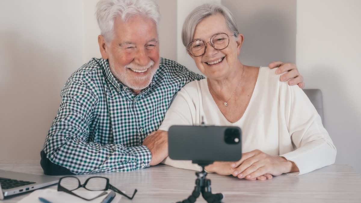 Video call concept. Elderly couple sitting at home talking remotely with family or friends on mobile phone webcam, modern senior handsome couple.