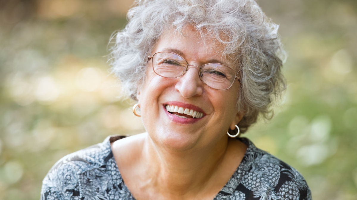 Portrait of senior woman smiling and looking at camera. Cheerful mature woman wearing eyeglasses in the park.